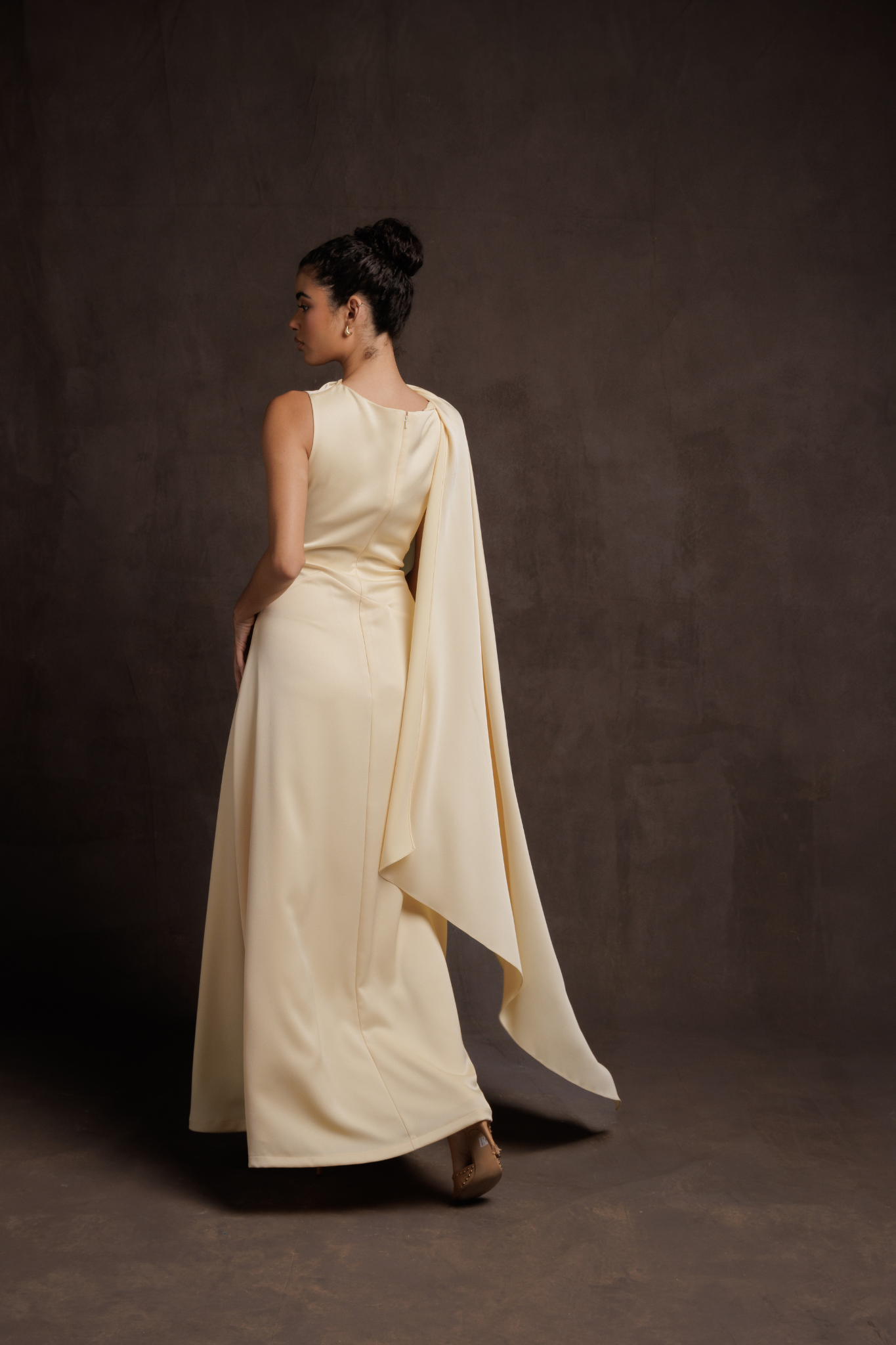 Woman wearing a long, light-colored dress with a cape against a dark background