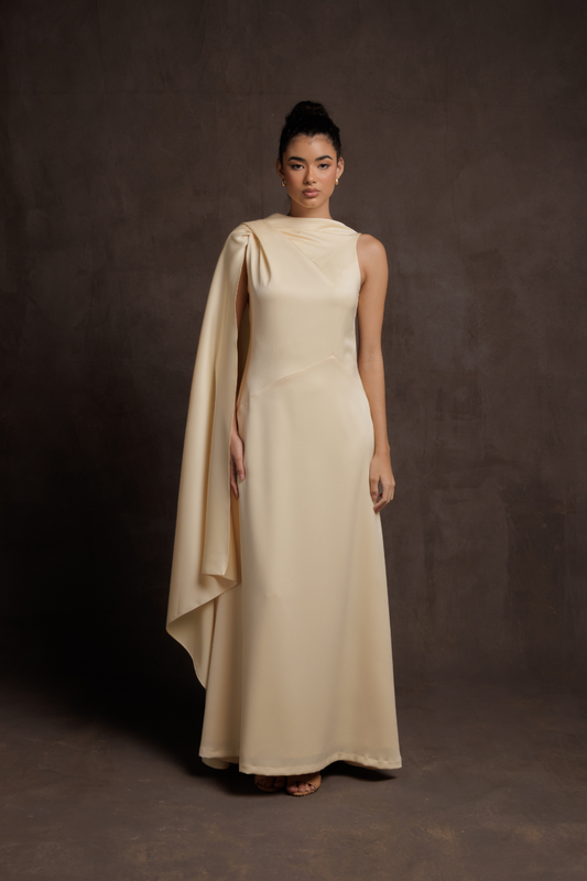 Woman wearing a beige evening gown with a draped effect on a dark background