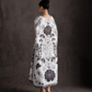 Woman wearing a long, white dress with black floral patterns against a dark background