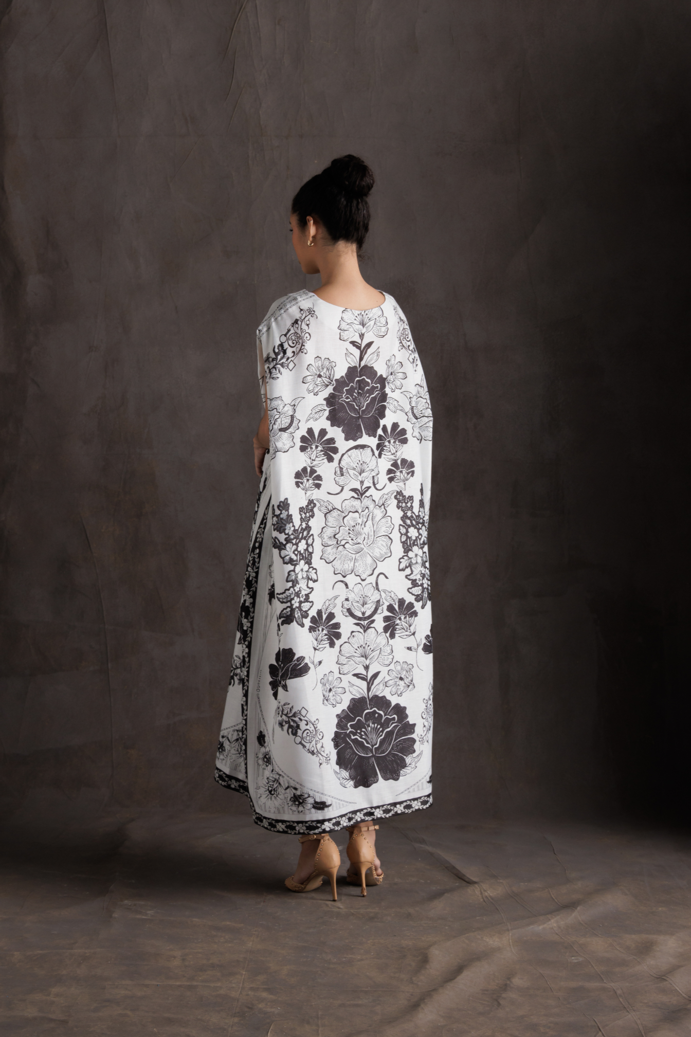 Woman wearing a long, white dress with black floral patterns against a dark background