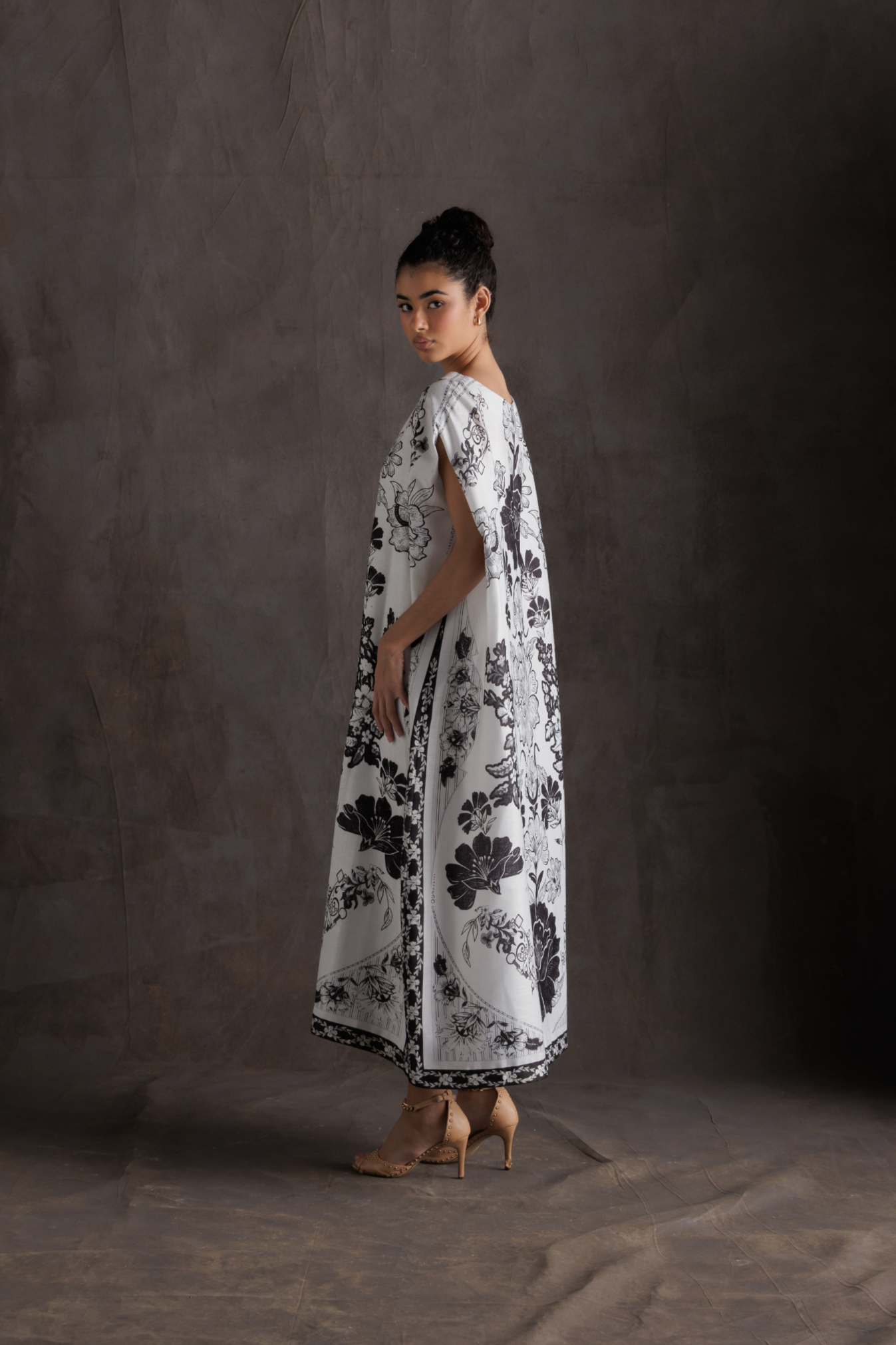 Woman wearing a white dress with black floral pattern against a dark background